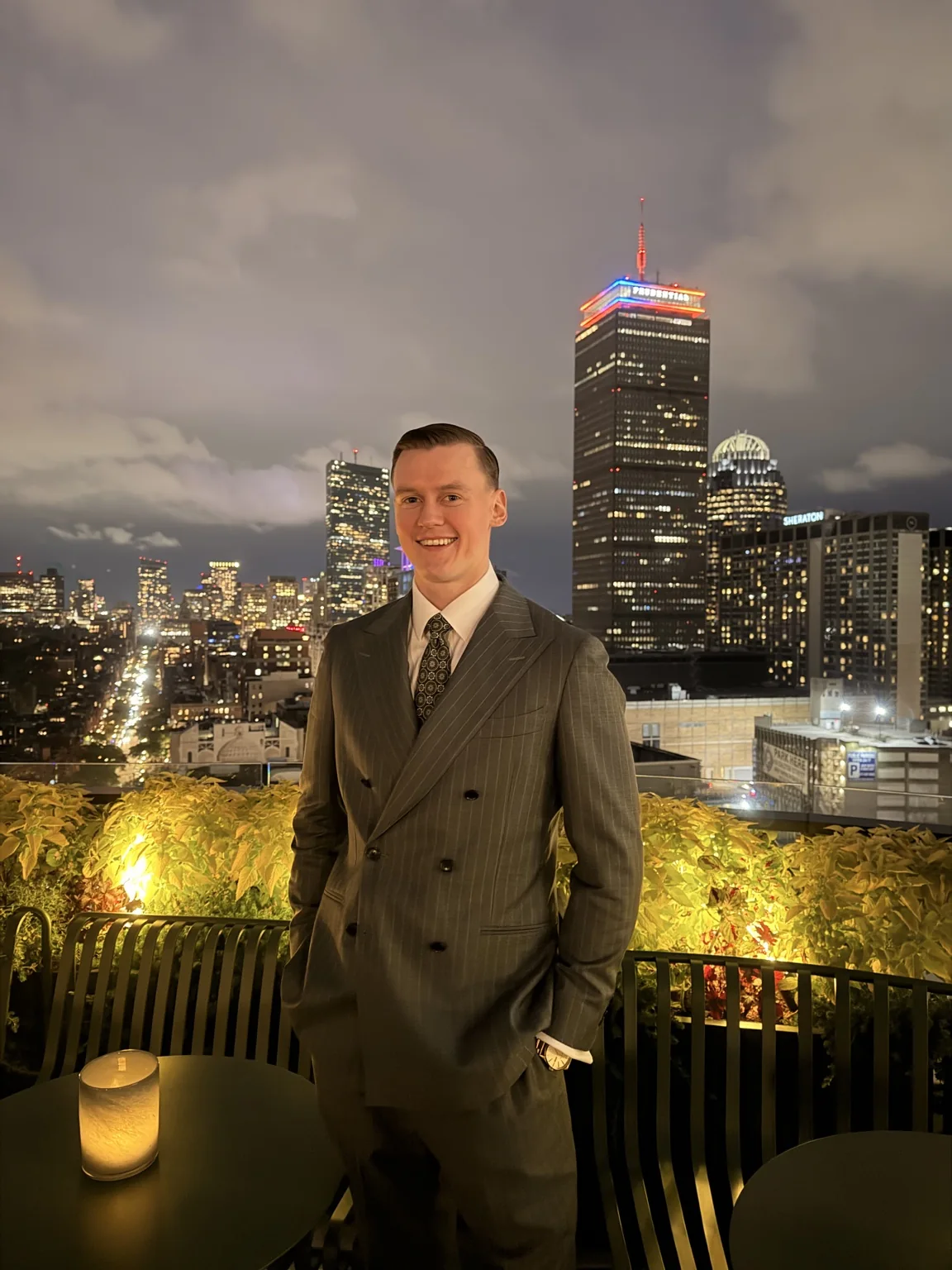 Joseph Dion smiling in a gray suit with the Boston skyline behind him.